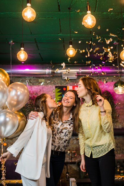 Jeunes amis souriants donnant un baiser à son amie en fête