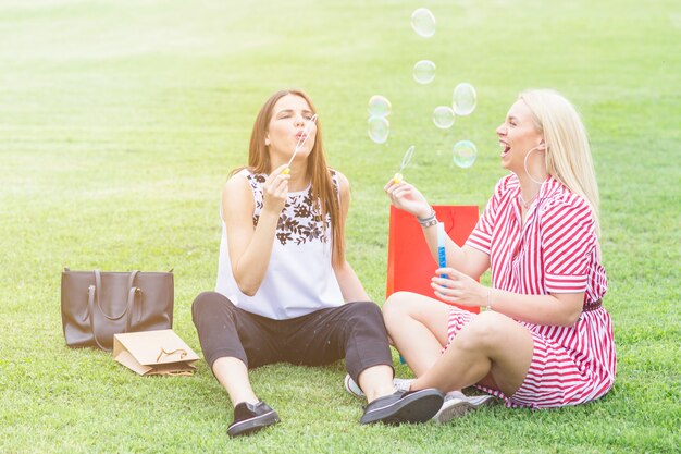 Jeunes belles femmes, assis sur la pelouse, soufflant des bulles avec la baguette bulle