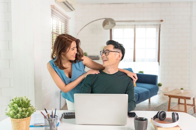 Les jeunes collègues de couple asiatique joyeux travaillent avec un ordinateur portable à l'intérieur du bureau en parlant les uns avec les autres.