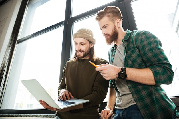 Jeunes collègues hommes concentrés au bureau à l'aide d'un ordinateur portable