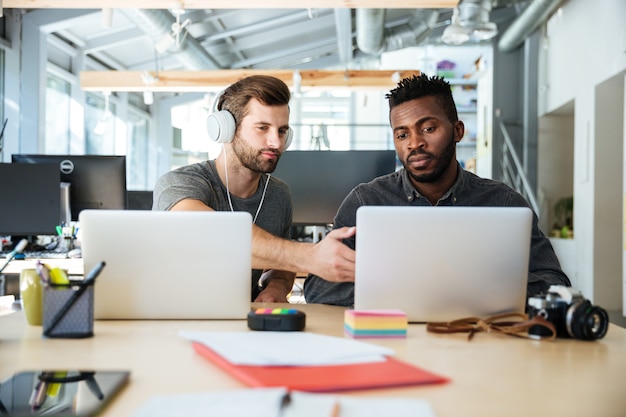 Photo gratuite jeunes collègues sérieux assis dans le coworking de bureau