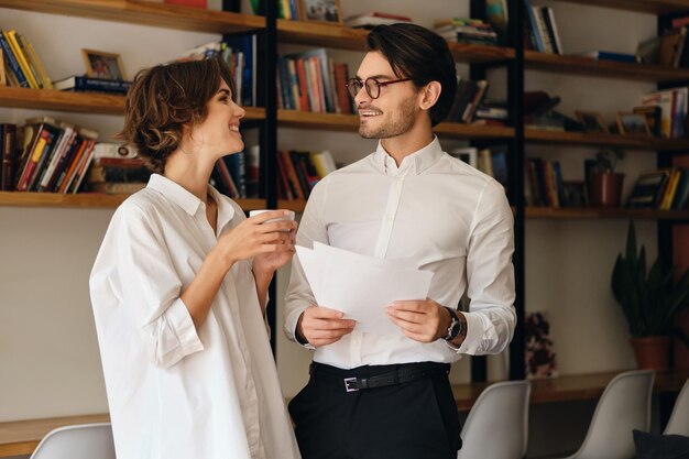 Jeunes collègues de travail attrayants se regardant joyeusement tout en travaillant ensemble dans un bureau moderne