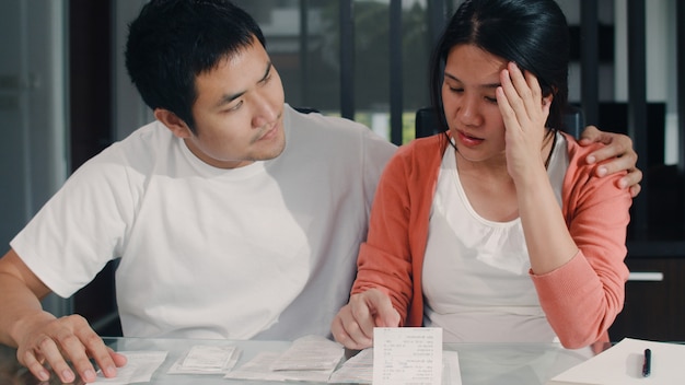 Jeunes couples de femmes enceintes asiatiques enregistrent leurs revenus et leurs dépenses à la maison. Maman inquiète, sérieuse, stressée tout en enregistrant un budget, une taxe, un document financier dans le salon à la maison.