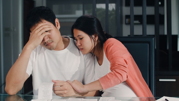 Jeunes couples de femmes enceintes asiatiques enregistrent leurs revenus et leurs dépenses à la maison. Papa inquiet, sérieux, stressé tout en enregistrant un budget, une taxe, un document financier dans le salon à la maison.