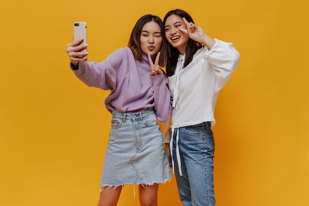 Les jeunes femmes asiatiques brunes prennent le selfie sur le mur orange