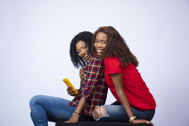 Jeunes femmes assises ensemble se sentant excitées, se tenant et un téléphone