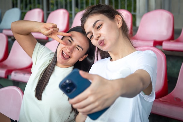 Photo gratuite des jeunes femmes athlétiques joyeuses se prenant un selfie avec leur smartphone dans la tribune.