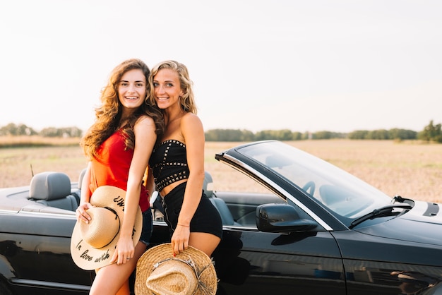 Jeunes femmes avec des chapeaux près du cabriolet noir