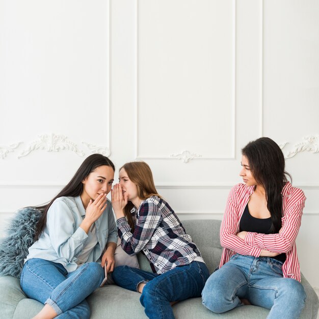 Jeunes femmes chuchotant derrière un ami