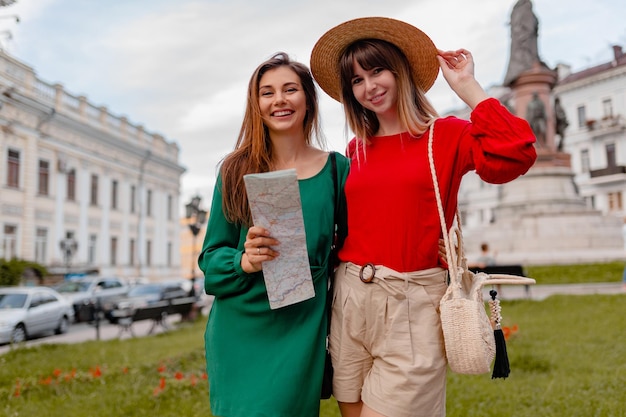 Photo gratuite jeunes femmes élégantes voyageant ensemble en europe vêtues d'une tenue à la mode printanière et d'accessoires souriants heureux amis s'amusant tenant la carte