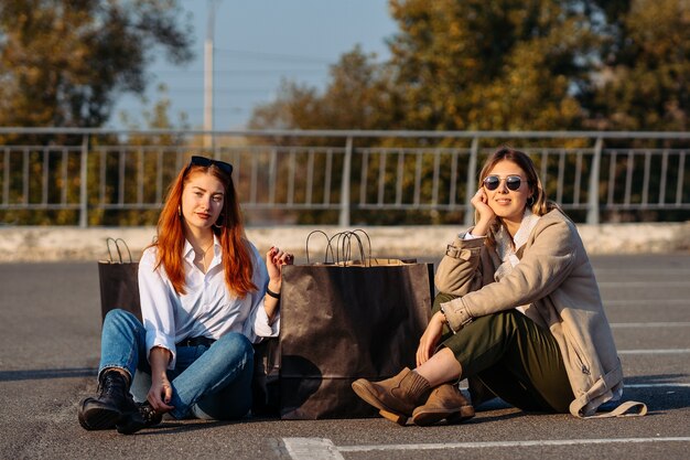 Jeunes femmes de la mode avec des sacs assis sur un parking