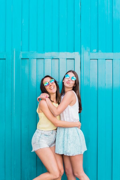 Jeunes femmes souriantes et étreignant près du mur bleu