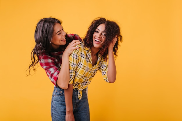 Les jeunes filles modernes aux cheveux bouclés foncés de bonne humeur apprécient les conversations décontractées. Portrait à l'intérieur de belles femmes avec des sourires blancs comme neige.