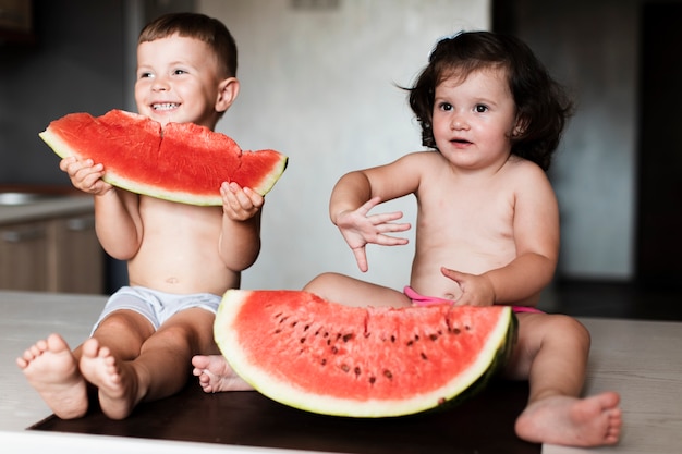 Jeunes frères et sœurs mangeant des tranches de melon d'eau