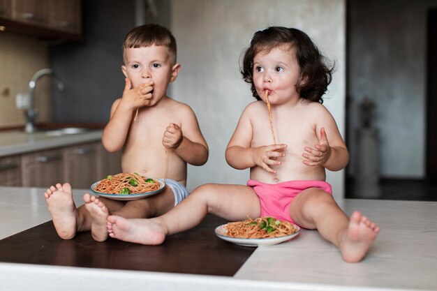 Jeunes frères et soeurs en train de manger des pâtes