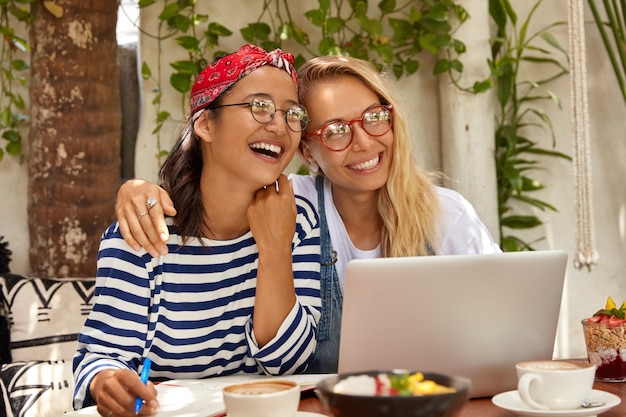 Photo gratuite des jeunes gais et insouciants s'embrassent, ont des relations amicales, rient joyeusement, regardent un programme intéressant sur internet