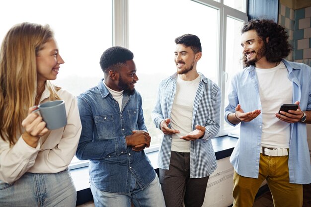 De jeunes gens d'affaires joyeux ont une conversation pendant la pause-café au bureau