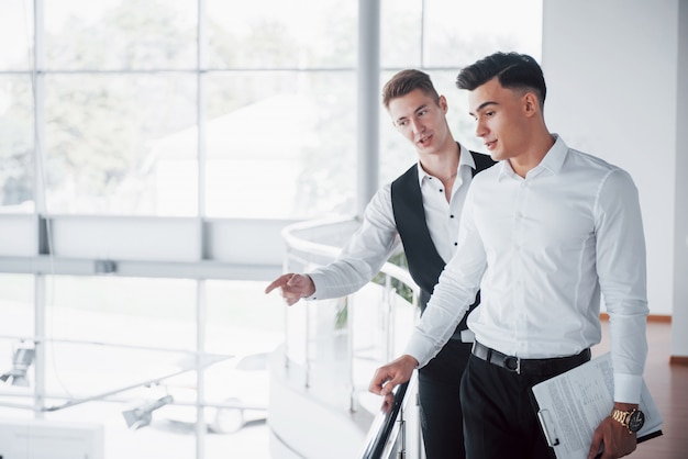 Les jeunes gens d'affaires à la recherche de documents et de produits debout à la balustrade du bureau