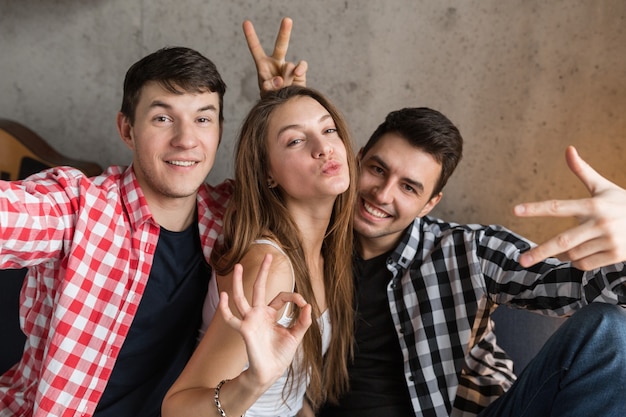 Jeunes heureux faisant une photo de selfie drôle, assis sur un canapé