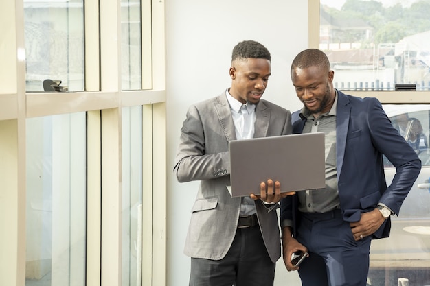 Jeunes hommes d'affaires debout ensemble tenant un ordinateur portable, discutant d'affaires