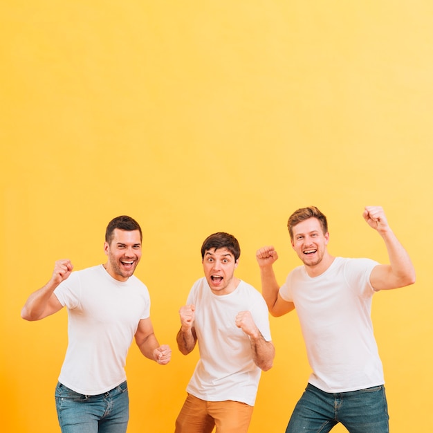 Jeunes hommes excités serrant leur poing debout contre un fond jaune