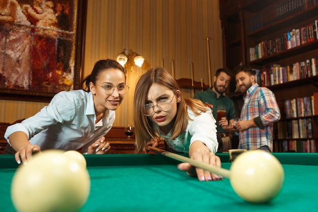 Jeunes hommes et femmes souriants jouant au billard au bureau ou à la maison après le travail. Collègues de travail impliqués dans des activités récréatives. Amitié, activité de loisirs, concept de jeu.