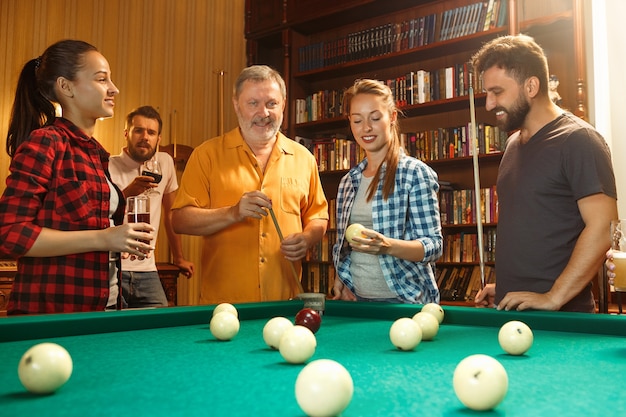 Jeunes hommes et femmes souriants jouant au billard au bureau ou à la maison après le travail. Collègues de travail impliqués dans des activités récréatives