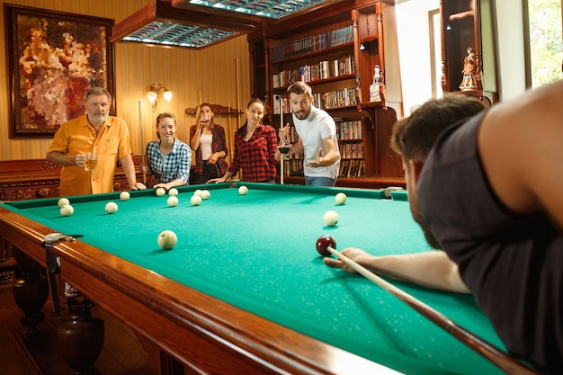 Jeunes hommes et femmes souriants jouant au billard au bureau ou à la maison après le travail. Collègues de travail impliqués dans des activités récréatives