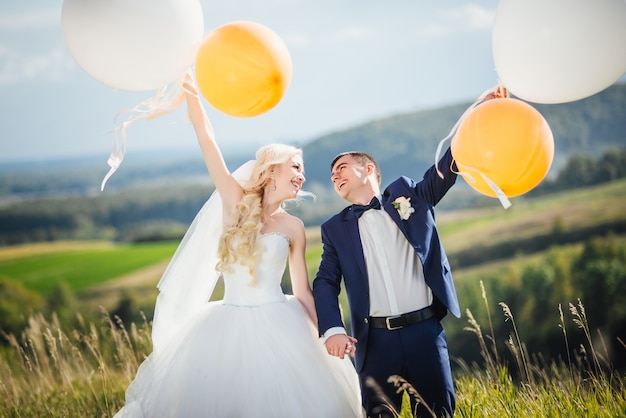 Photo gratuite jeunes mariés heureux et souriants avec des ballons d'hélium s'amusant après la cérémonie de mariage