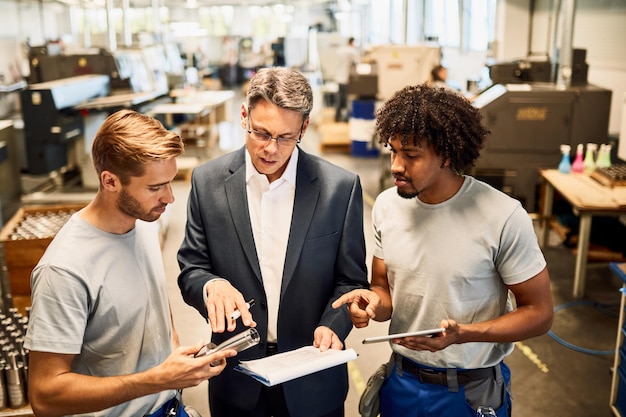 Photo gratuite jeunes métallurgistes coopérant avec leur manager lors de la lecture de rapports dans un bâtiment industriel