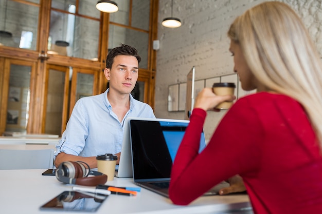 Les jeunes occupés assis à table face à face, travaillant à l'ordinateur portable dans le bureau de travail en commun