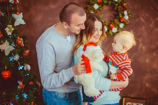 Jeunes parents gais tiennent le petit enfant posant devant un arbre de Noël