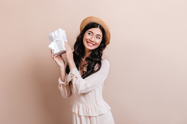 Jocund femme chinoise tenant un cadeau d'anniversaire. Femme asiatique assez bouclée posant avec un cadeau.