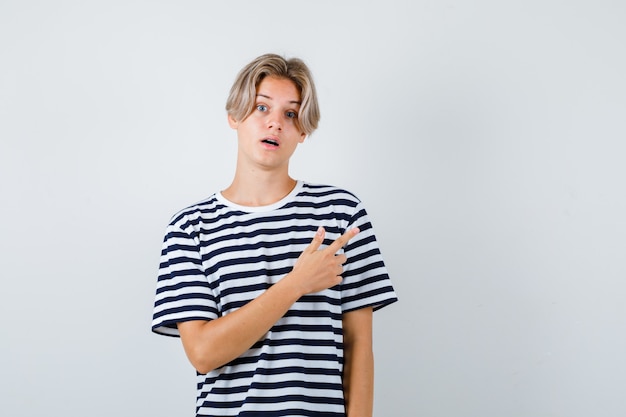 Joli adolescent pointant vers le coin supérieur droit en t-shirt rayé et ayant l'air perplexe. vue de face.