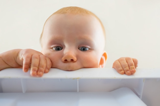 Joli bébé affamé aux cheveux roux mordant le panneau en plastique. Vue rapprochée du nouveau-né curieux à la recherche de la table et le tenant. Concept de l'enfance et de la petite enfance