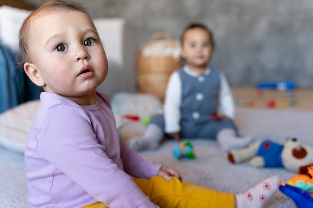 Joli bébé jouant sur le sol avec un jouet pendant que le bébé défocalisé joue avec un jouet