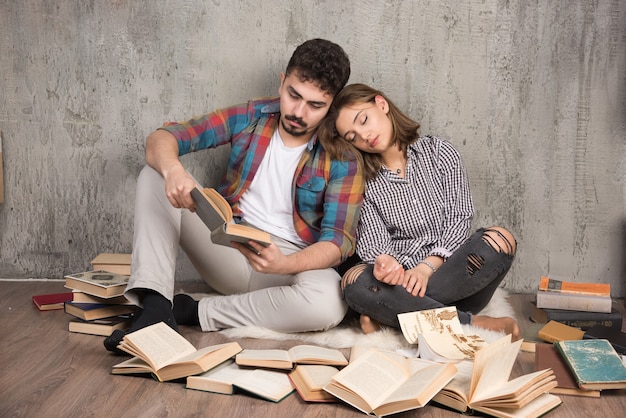 Photo gratuite joli couple assis sur le sol avec beaucoup de livres