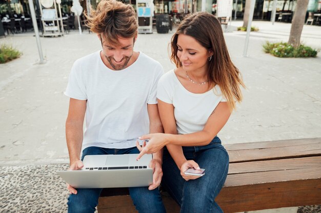 Joli couple sur un banc avec un ordinateur portable