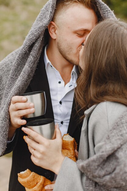 Joli couple dans un parc. Dame dans un manteau gris. Les gens avec un thermos et un croissant.