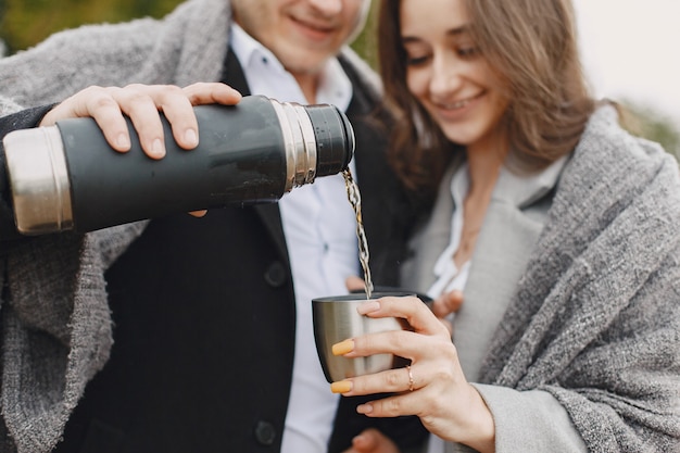 Joli couple dans un parc. Dame dans un manteau gris. Les gens avec un thermos.