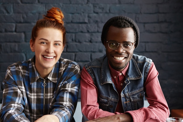 Photo gratuite joli couple interracial se détendre à l'intérieur, assis contre le mur de briques noires