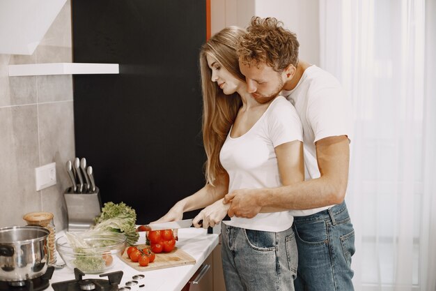 Joli couple à la maison. Dame en t-shirt blanc. Les gens préparent une salade.