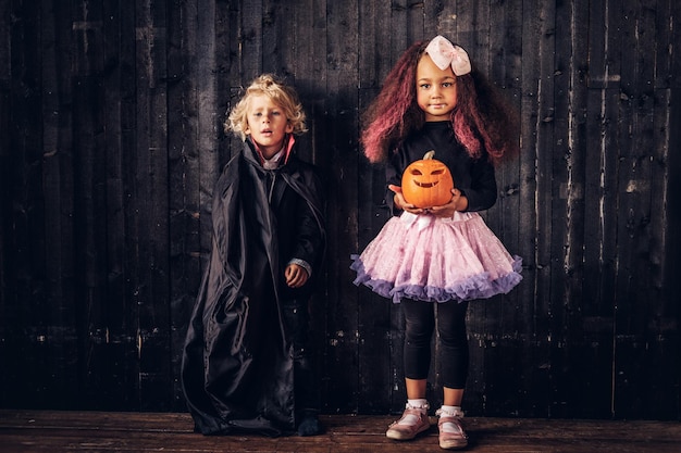 Photo gratuite joli couple de petits enfants en costumes effrayants posant dans une vieille maison. notion d'halloween.