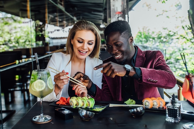 Joli couple s'amusant en mangeant des rouleaux de sushi au restaurant sur une terrasse moderne.