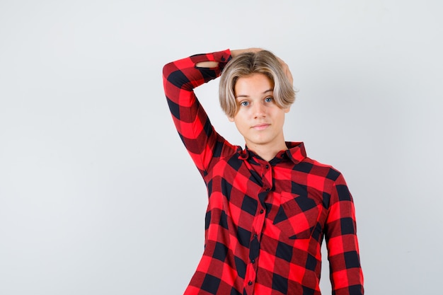 Joli garçon adolescent en chemise à carreaux avec la main derrière la tête et l'air intelligent, vue de face.