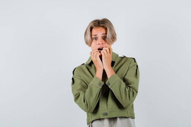 Joli garçon adolescent gardant les mains près de la bouche ouverte en veste verte et l'air terrifié. vue de face.