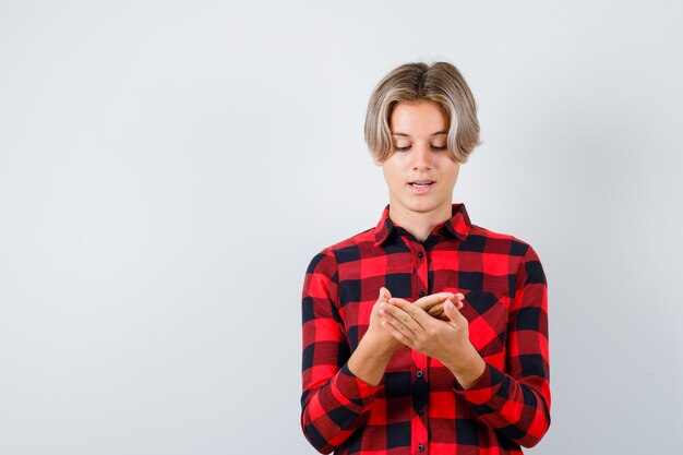 Joli garçon adolescent regardant sa paume en chemise à carreaux et ayant l'air plein d'espoir, vue de face.