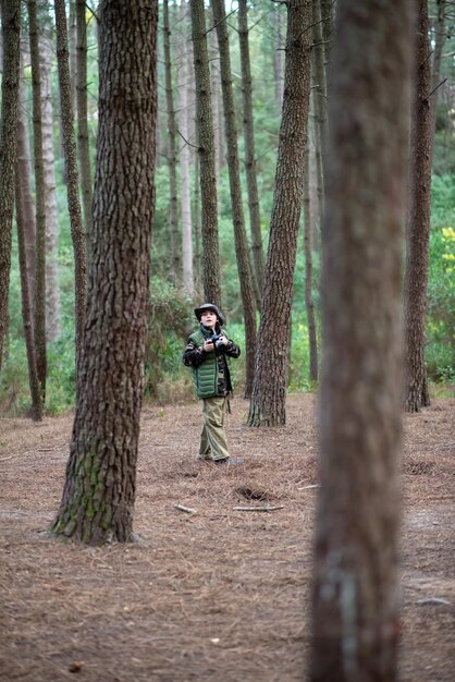 Joli garçon avec caméra en forêt. Écolier en manteau et panama prenant des photos, marchant. Enfance, nature, concept de loisirs