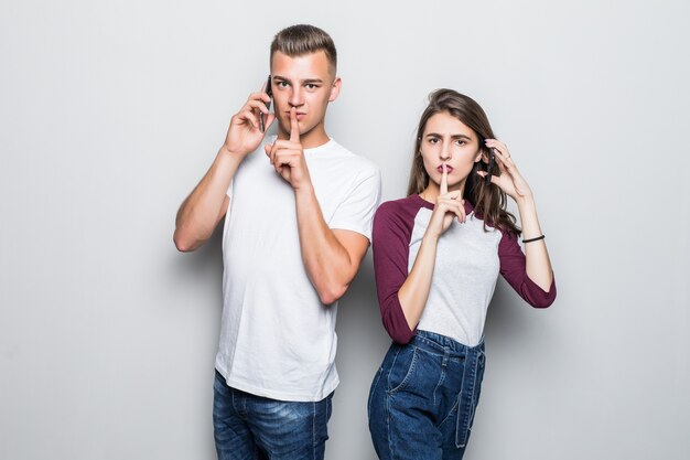 Joli jeune beau couple garçon et fille demandent à être silencieux pendant un appel téléphonique isolé sur blanc