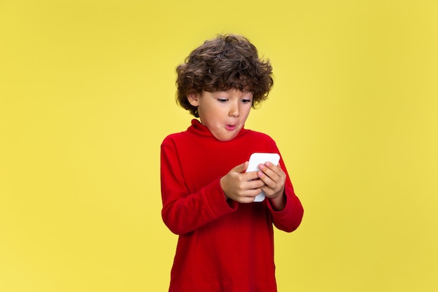 Joli jeune garçon bouclé en vêtements rouges sur l'amusement de l'expression de l'enfance du mur jaune